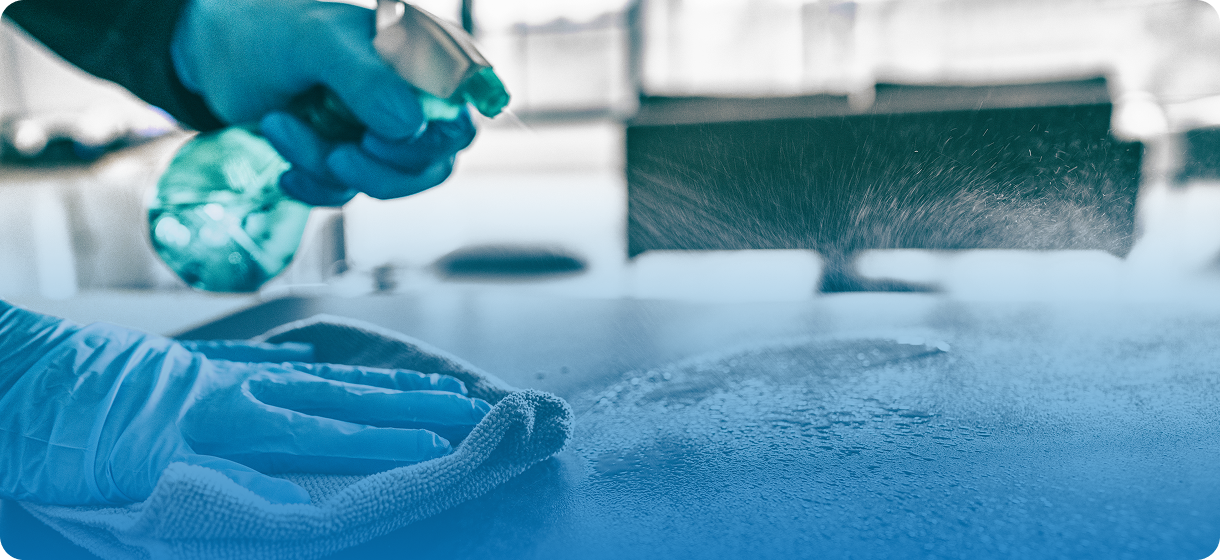 Gloved hands cleaning surface with spray bottle.