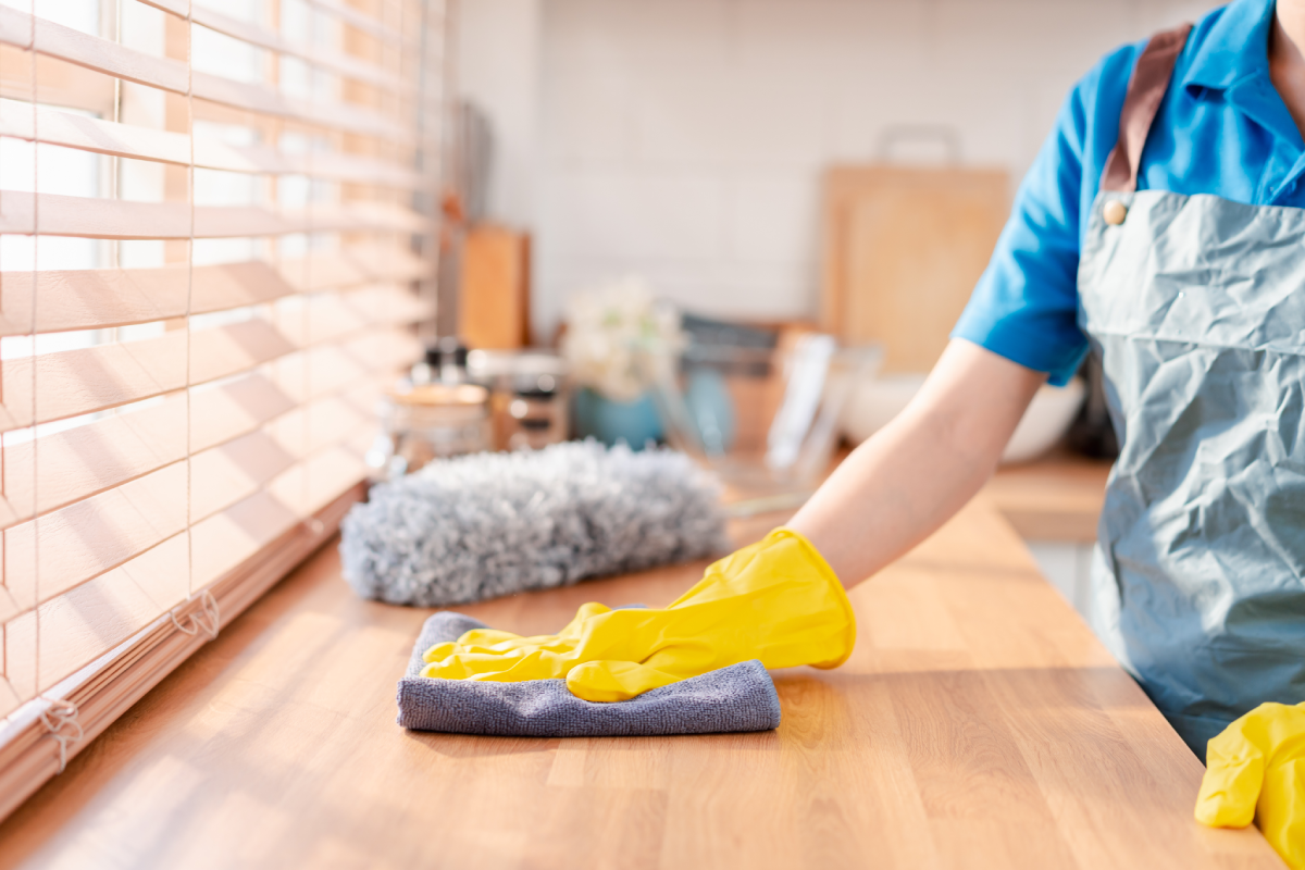 Person cleaning countertop with yellow gloves.